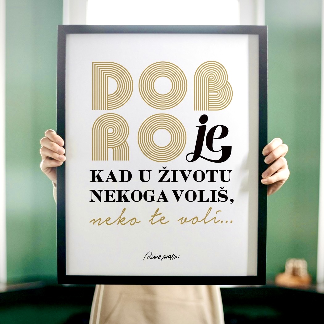 Dino Merlin poster/dekoracija za zid u bijeloj boji i dizajnom stiha 'Dobro je kad u životu nekoga voliš, neko te voli' u gold varijanti naslonjen na zid pored česme tradicionalnog izgleda