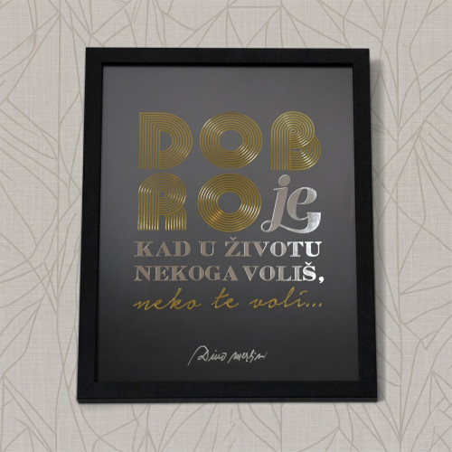 Elegantna dekoracija za zid s natpisom "Dobro je kad u životu nekoga voli&scaron;, neko te voli" s slovima zlatne boje i s potpisom Dine Merlina na bijeloj pozadini. 