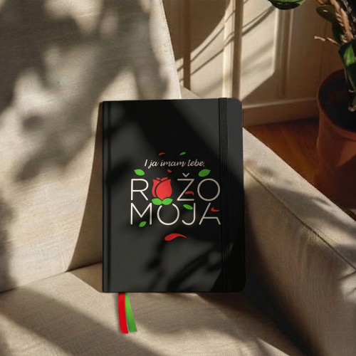 Crni premium rokovnik  "I ja imam tebe ružo moja" u ruci djevojke u bijeloj majici i frčkavom kosom. 