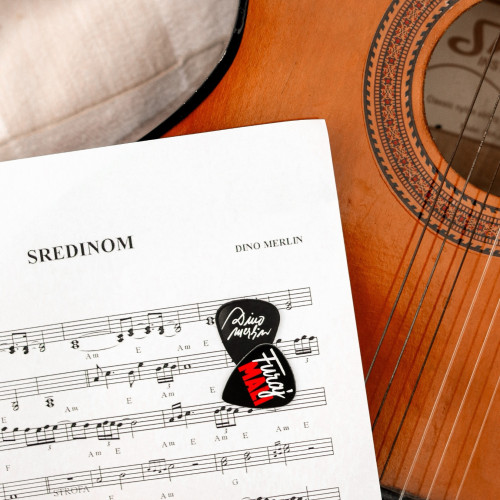 Crne trzalice za gitaru sa bijelo-crvenim printom ''Furaj mali'' inspirisane stihom iz pjesme Dine Merlina "Sredinom" sa istoimenog albuma na papiru sa notama i smeđom gitarom u pozadini.