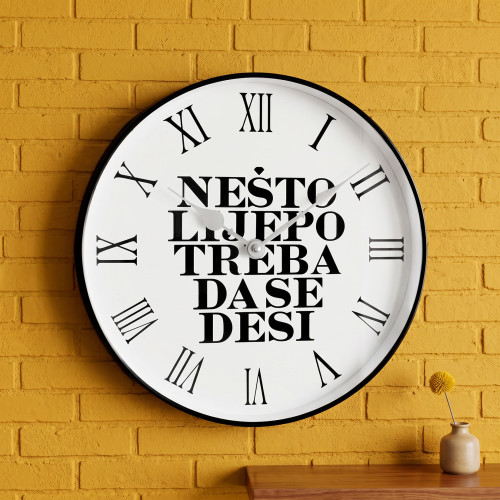 Elegantni crno-bijeli quartz zidni sat &ldquo;Ne&scaron;to lijepo treba da se desi&rdquo; na bijeloj pozadini.
