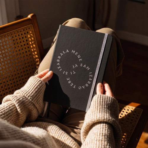 Crni premium rokovnik tvrdih korica &ldquo;Ti si izabrala mene, ja sam izabrao tebe&rdquo;, koji djevojka pažljivo izvlači iz torbe iz Dino Merlin kolekcije.