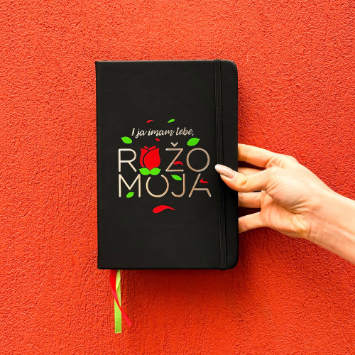 Crni premium rokovnik  "I ja imam tebe ružo moja" u ruci djevojke u bijeloj majici i frčkavom kosom. 