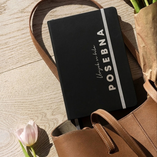 Crni premium rokovnik "Uvijek si bila posebna" s rukom djevojke koja drži &scaron;olju s kafom na bijelom stolu. 