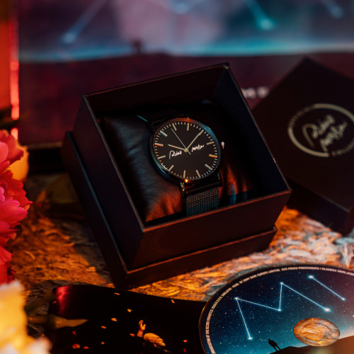 Crni unisex ručni sat sa bijelim potpisom Dine Merlina i indexima boje srebra na bijeloj pozadini.