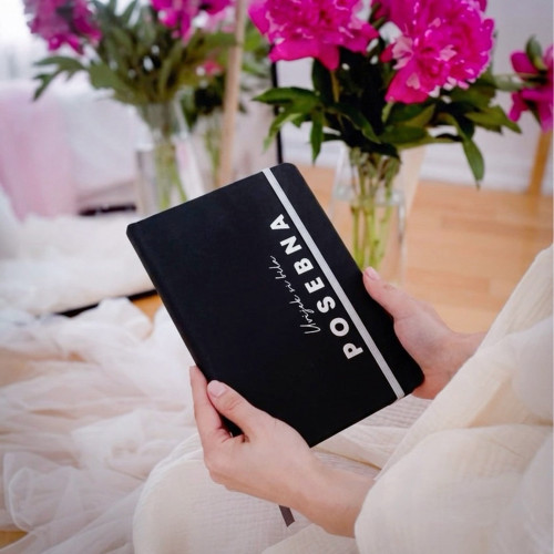 Crni premium rokovnik "Uvijek si bila posebna" s rukom djevojke koja drži &scaron;olju s kafom na bijelom stolu. 